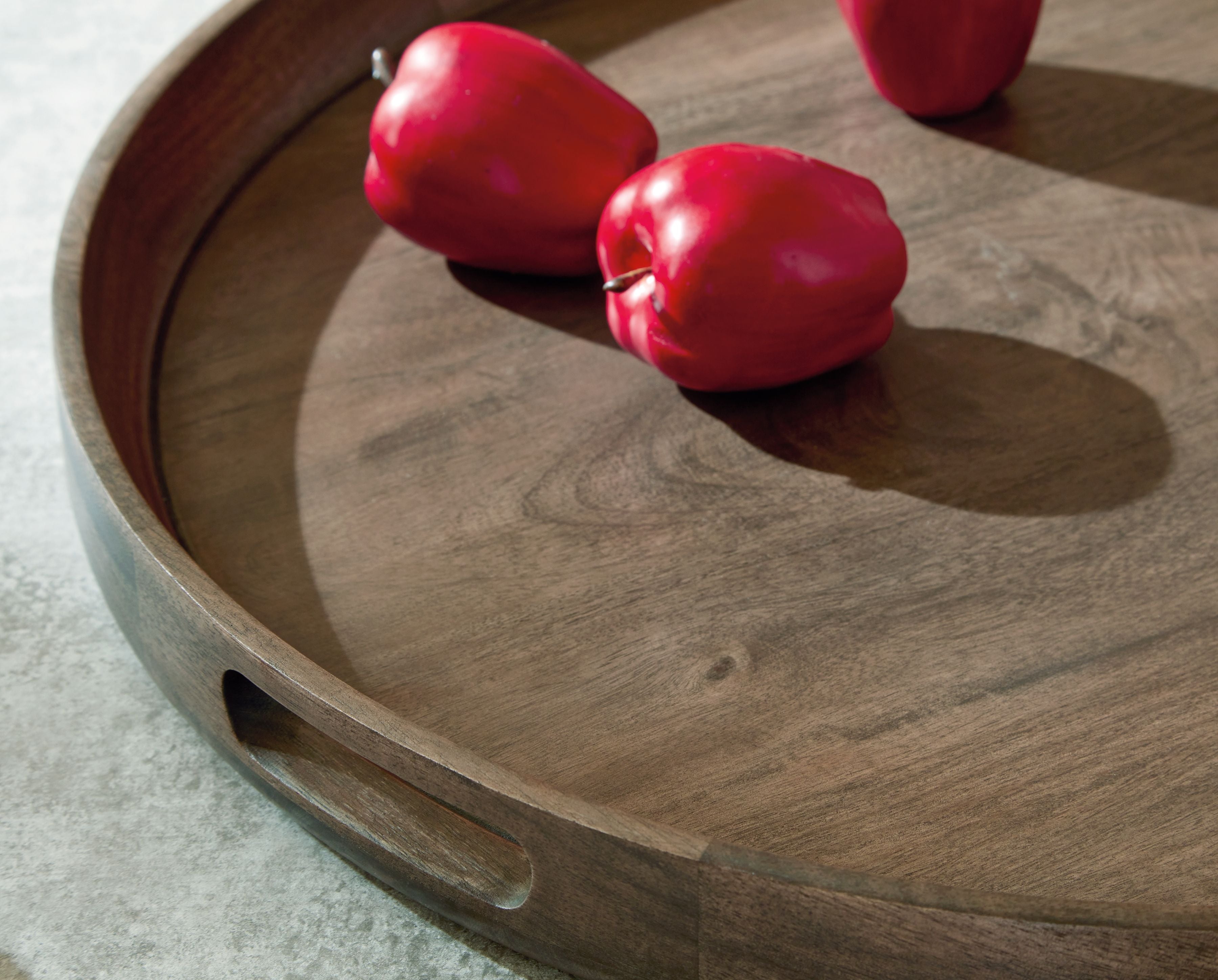Gray-brown wooden round tray with side handle cutout, holding red peppers
