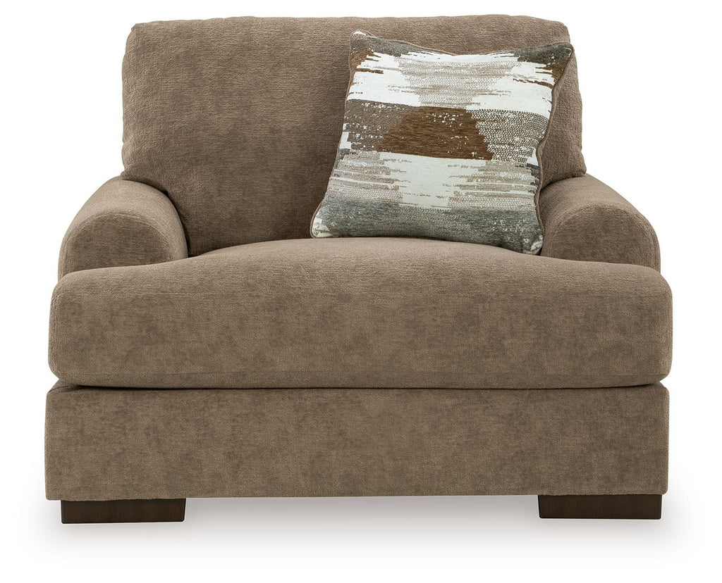Armchair in light brown fabric with deep seat, broad arms, and one patterned throw pillow