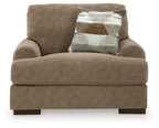 Armchair in light brown fabric with deep seat, broad arms, and one patterned throw pillow