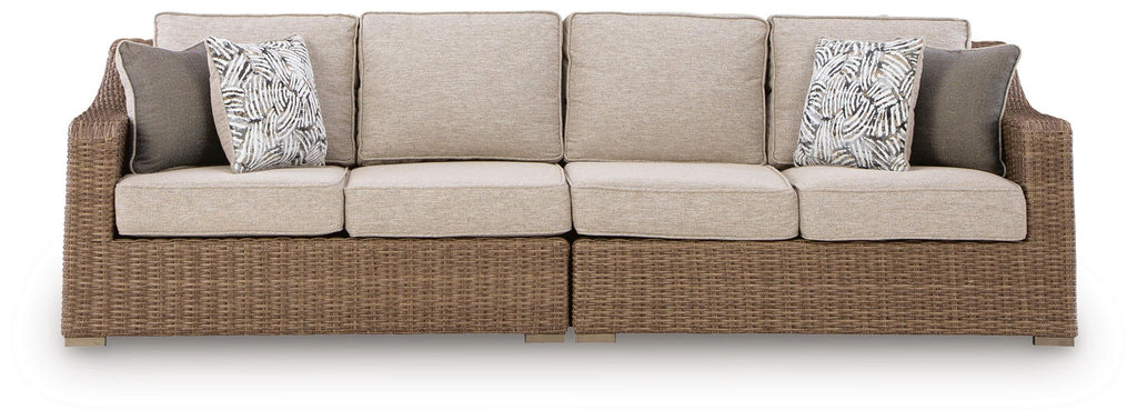 Beige loveseat with seat cushions and two patterned throw pillows, woven base.