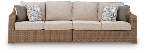 Beige loveseat with seat cushions and two patterned throw pillows, woven base.
