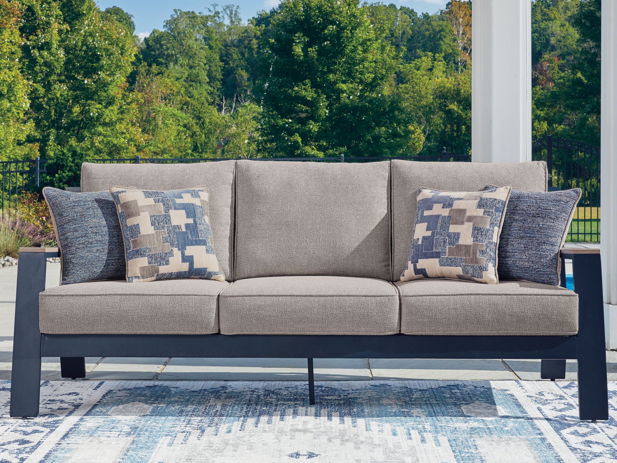Outdoor sofa with light gray seat cushions and two blue patterned throw pillows