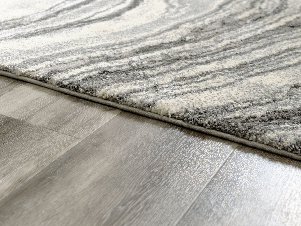 Rug edge close-up showing thick pile and dark gray border on gray surface.