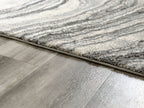 Rug edge close-up showing thick pile and dark gray border on gray surface.