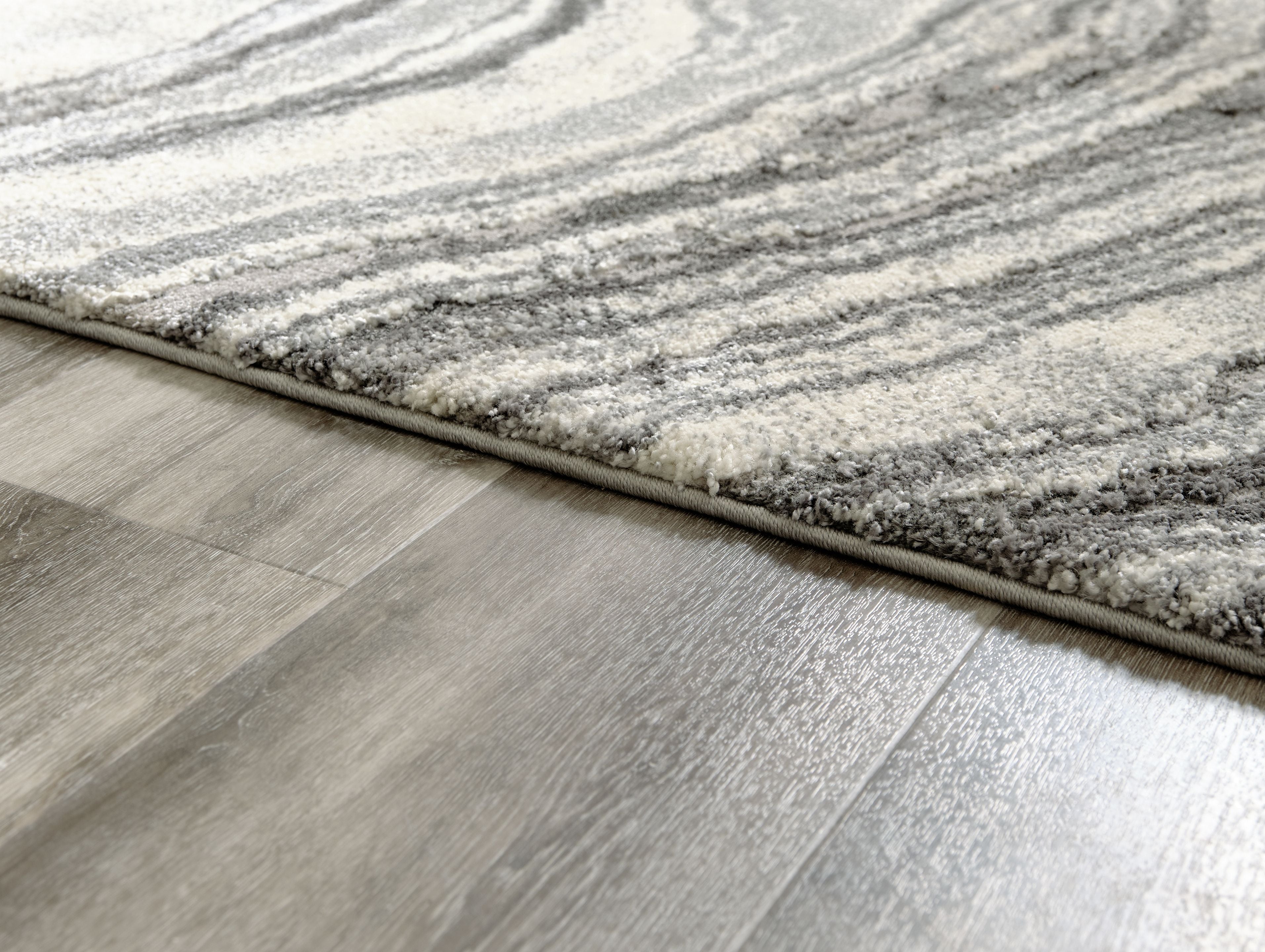 Rug edge close-up showing thick pile and dark gray border on gray surface.