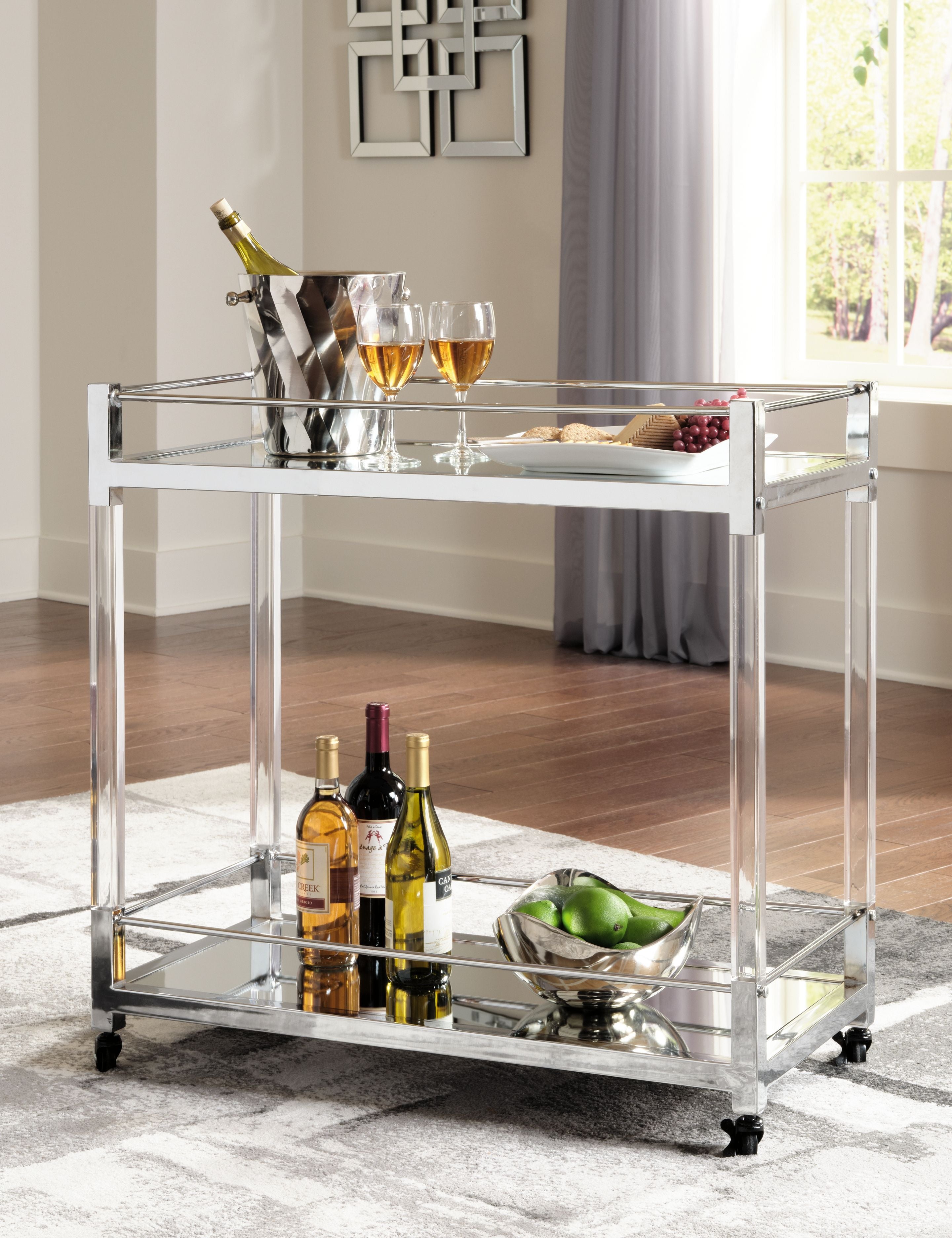 Clear glass bar cart with silver frame, holding bottles and a drink tray