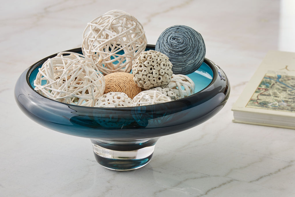 Teal blue glass bowl with dark rim, holding decorative shells and yarn balls