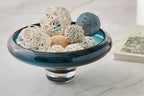 Teal blue glass bowl with dark rim, holding decorative shells and yarn balls