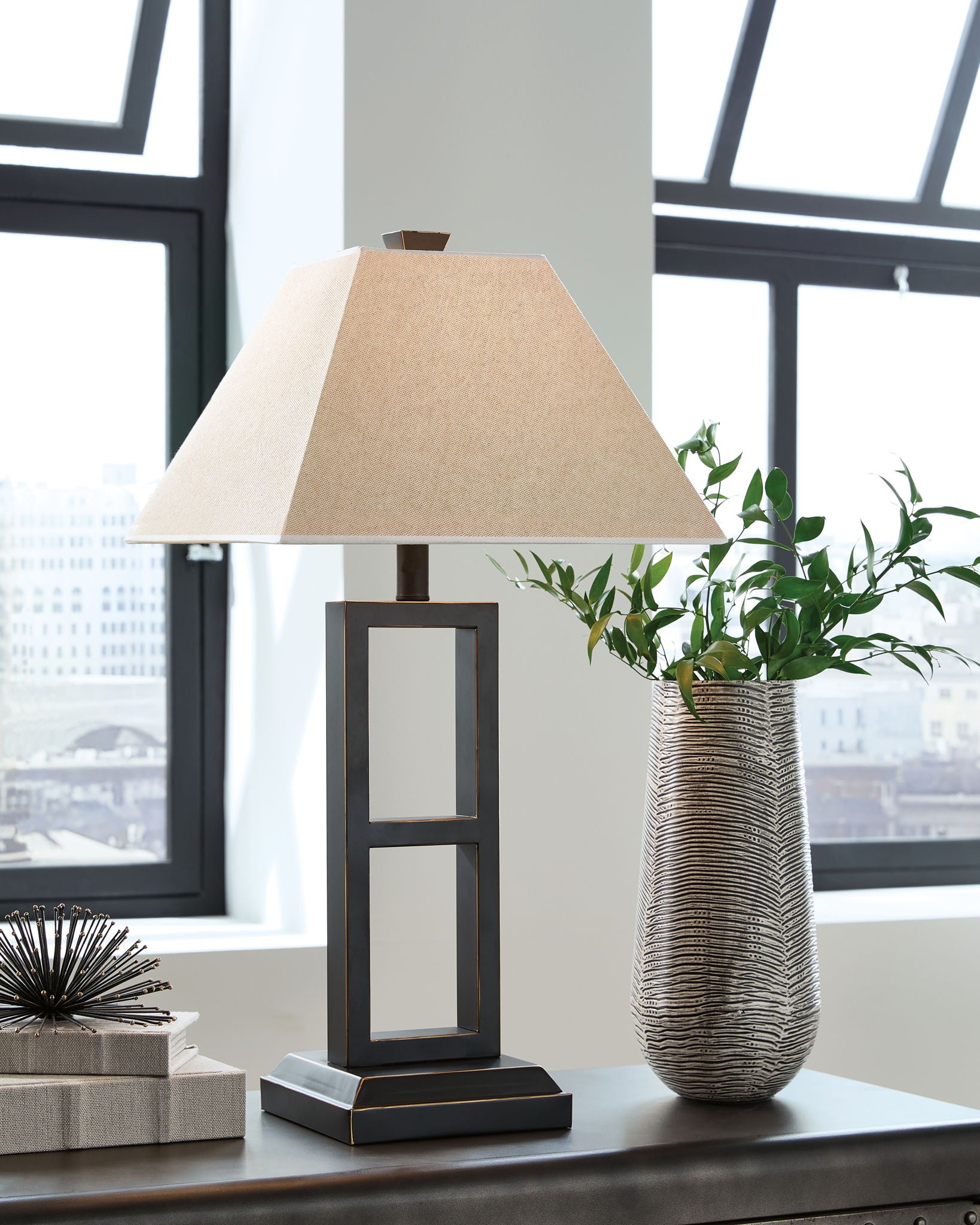 Black metal table lamp with tan fabric shade, glass window panels, on desk
