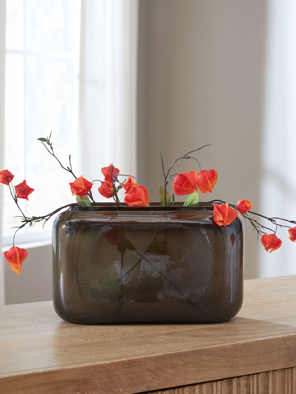 Sumner vase with dark brown glossy finish holding red flowers on a tabletop