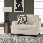 Beige upholstered living room chair with patterned throw pillow and square ottoman