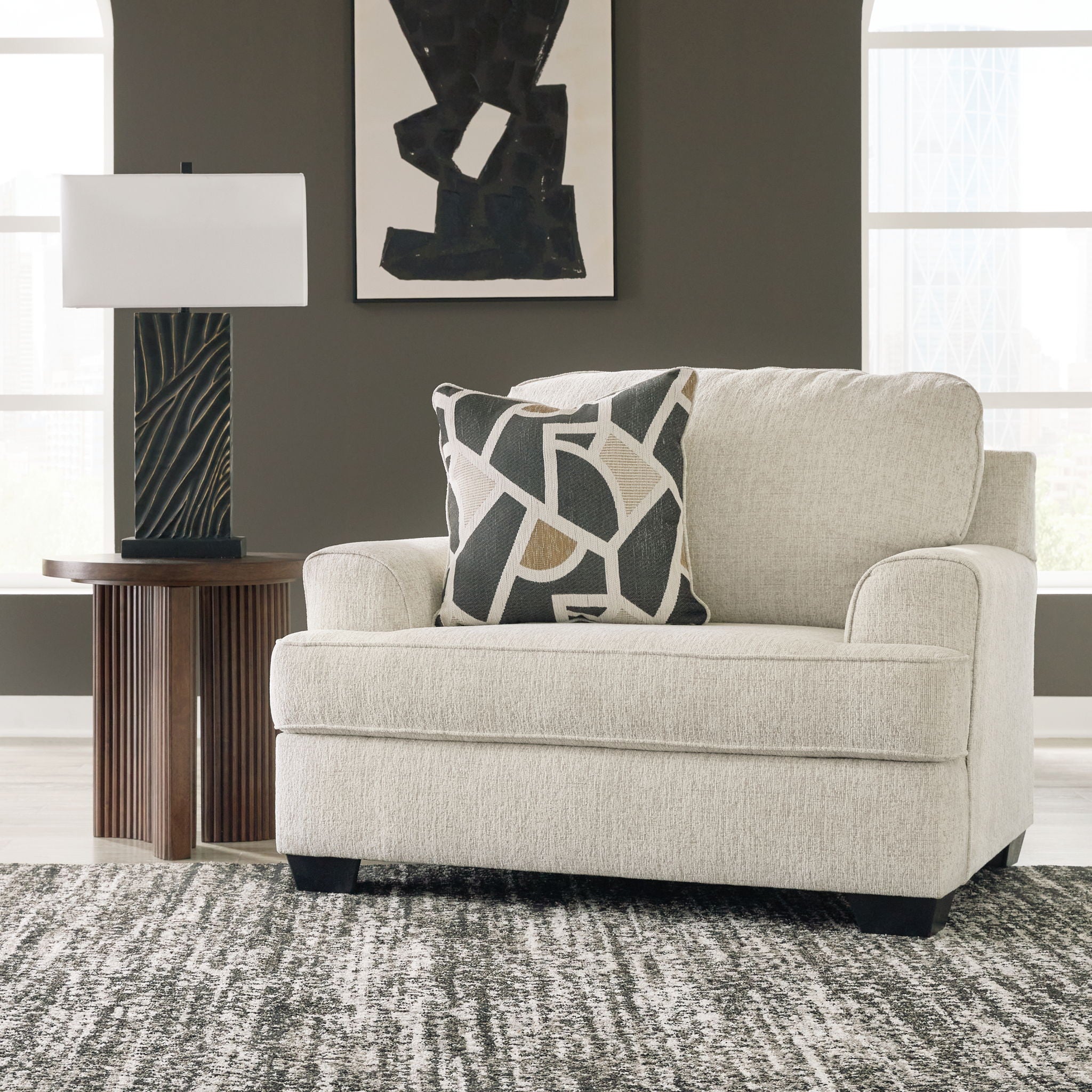 Beige upholstered living room chair with patterned throw pillow and square ottoman