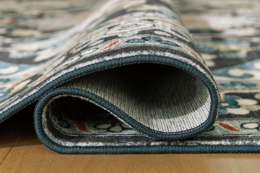 Washable area rug edge close-up with black pile and dark teal binding.