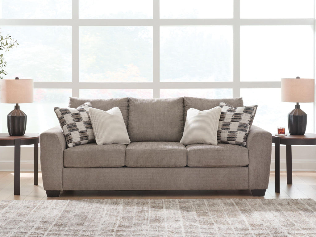 Light brown upholstered sofa with patterned and white accent pillows and three seats