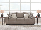 Light brown upholstered sofa with patterned and white accent pillows and three seats