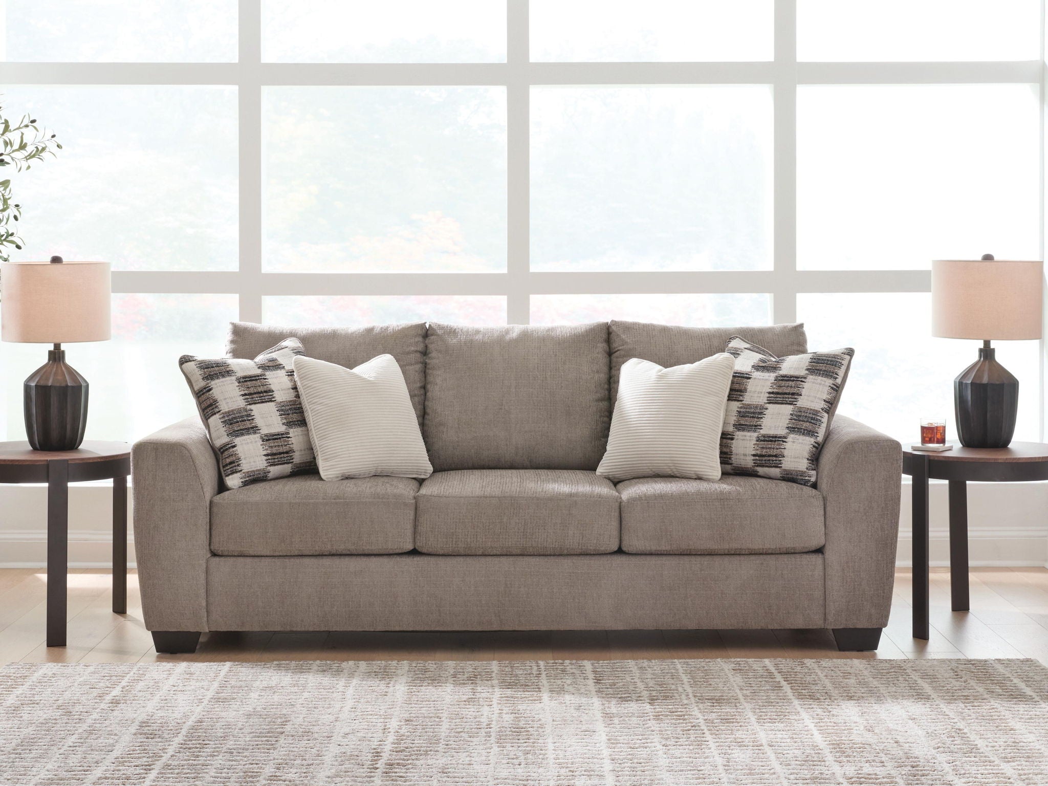 Light brown upholstered sofa with patterned and white accent pillows and three seats