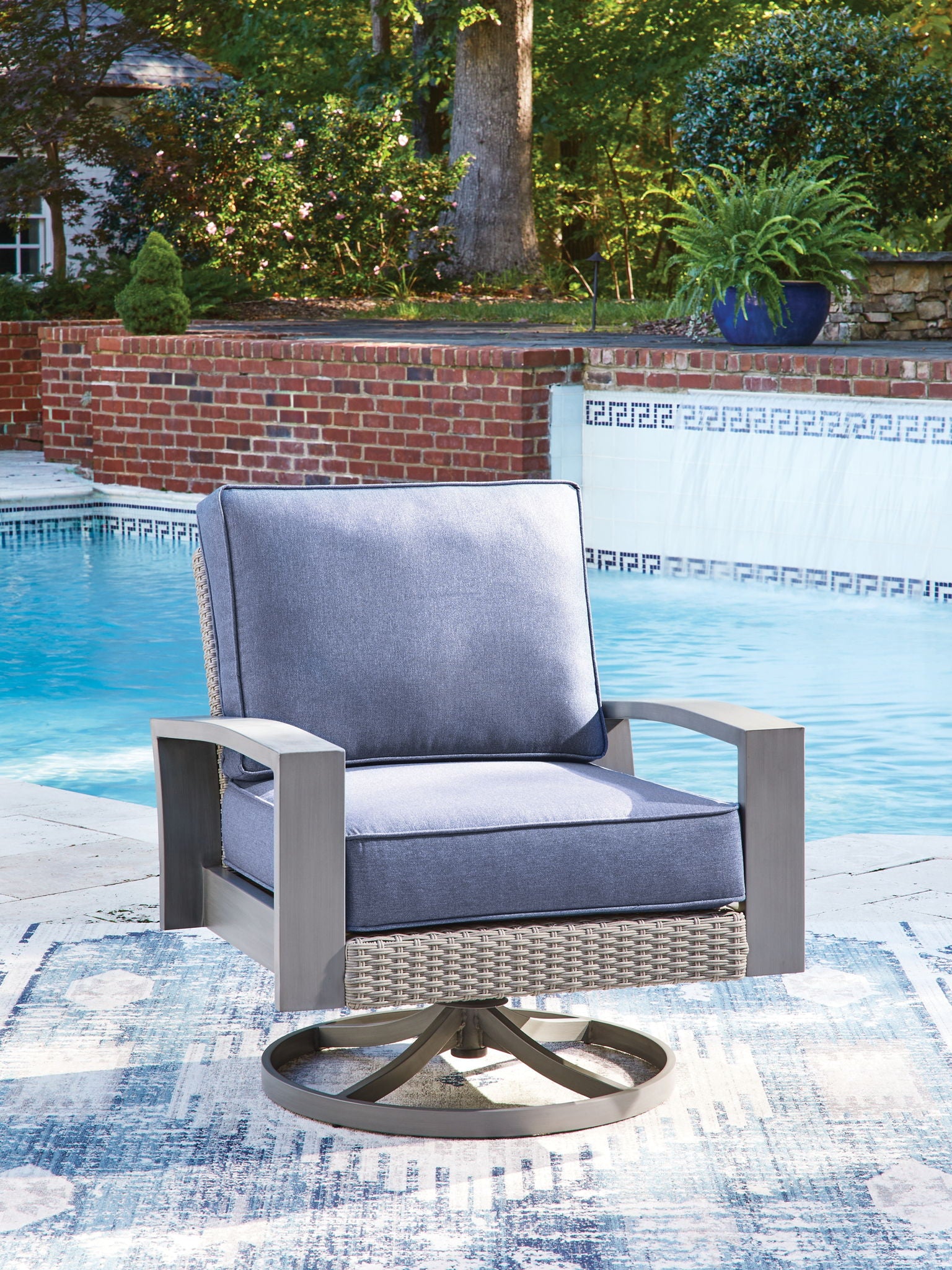 Outdoor swivel lounge chair with blue cushion and gray woven back and seat, round base