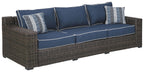 Brown wicker sofa with blue cushions and two striped throw pillows