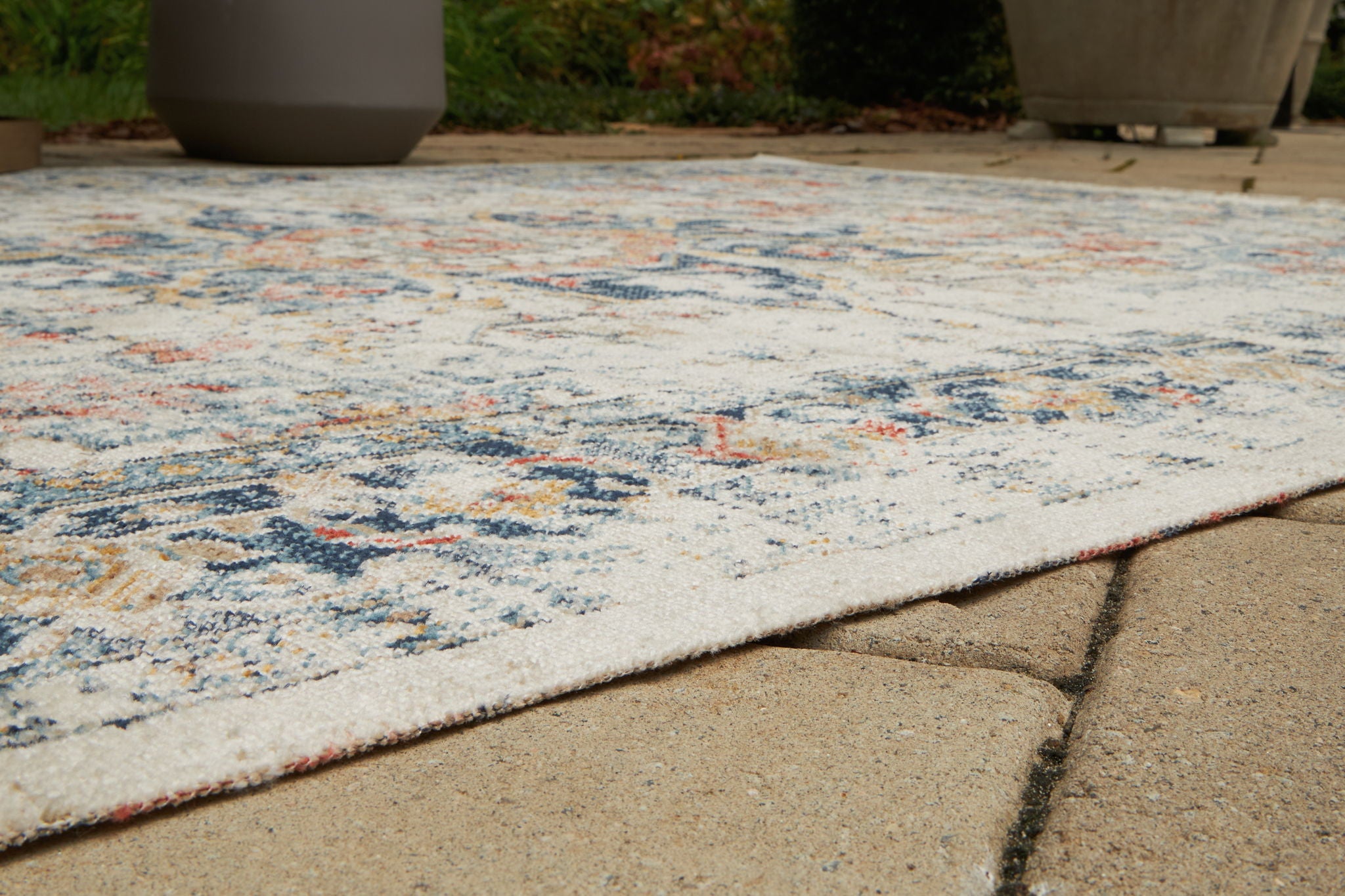 Multi-pattern area rug edge on patio, low pile with blue and orange distressed details