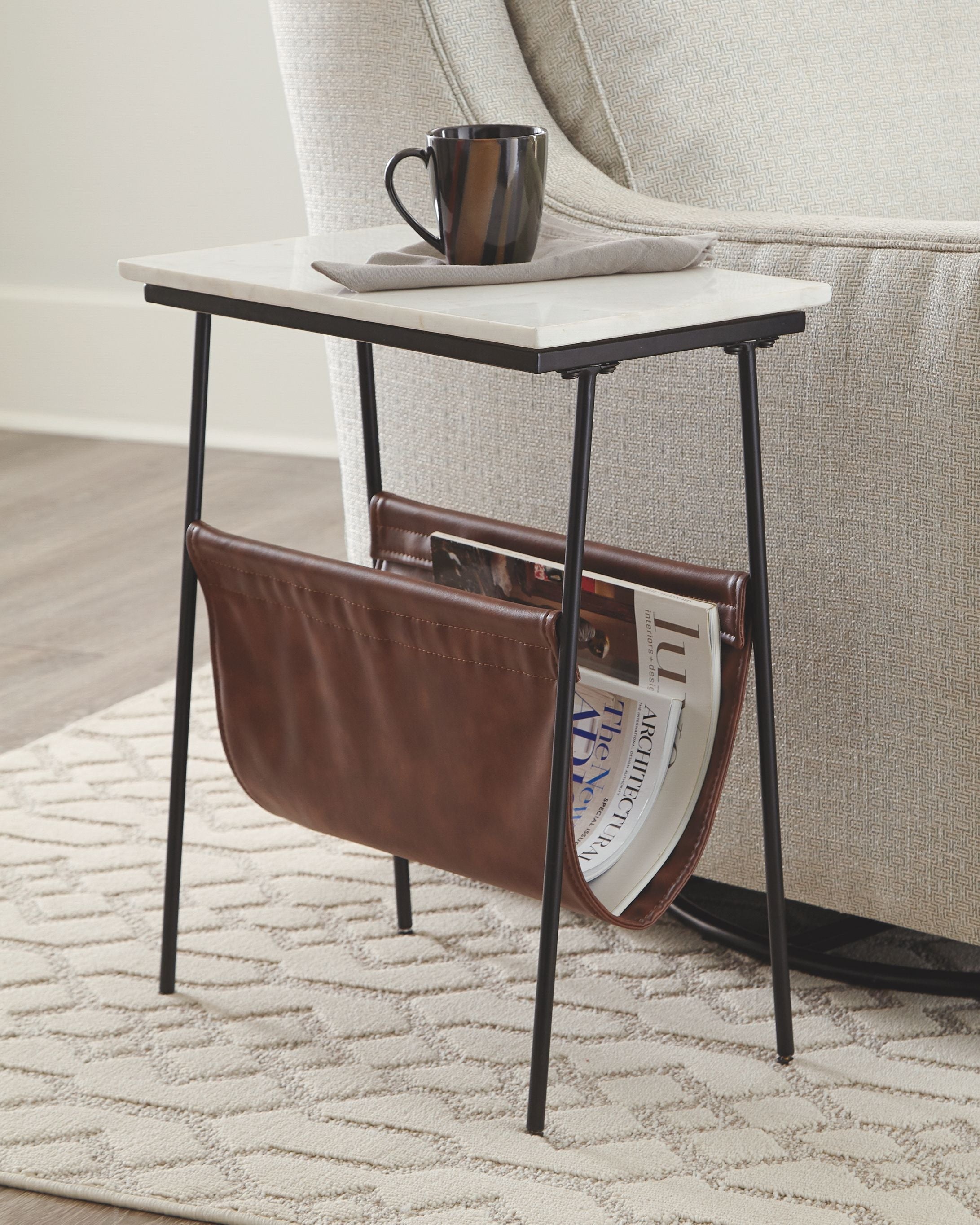 Accent table with white top, black frame, brown leather magazine holder and mug