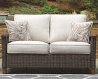 Outdoor loveseat with cushion, light beige upholstery, dark wicker base, leaf-pattern pillows