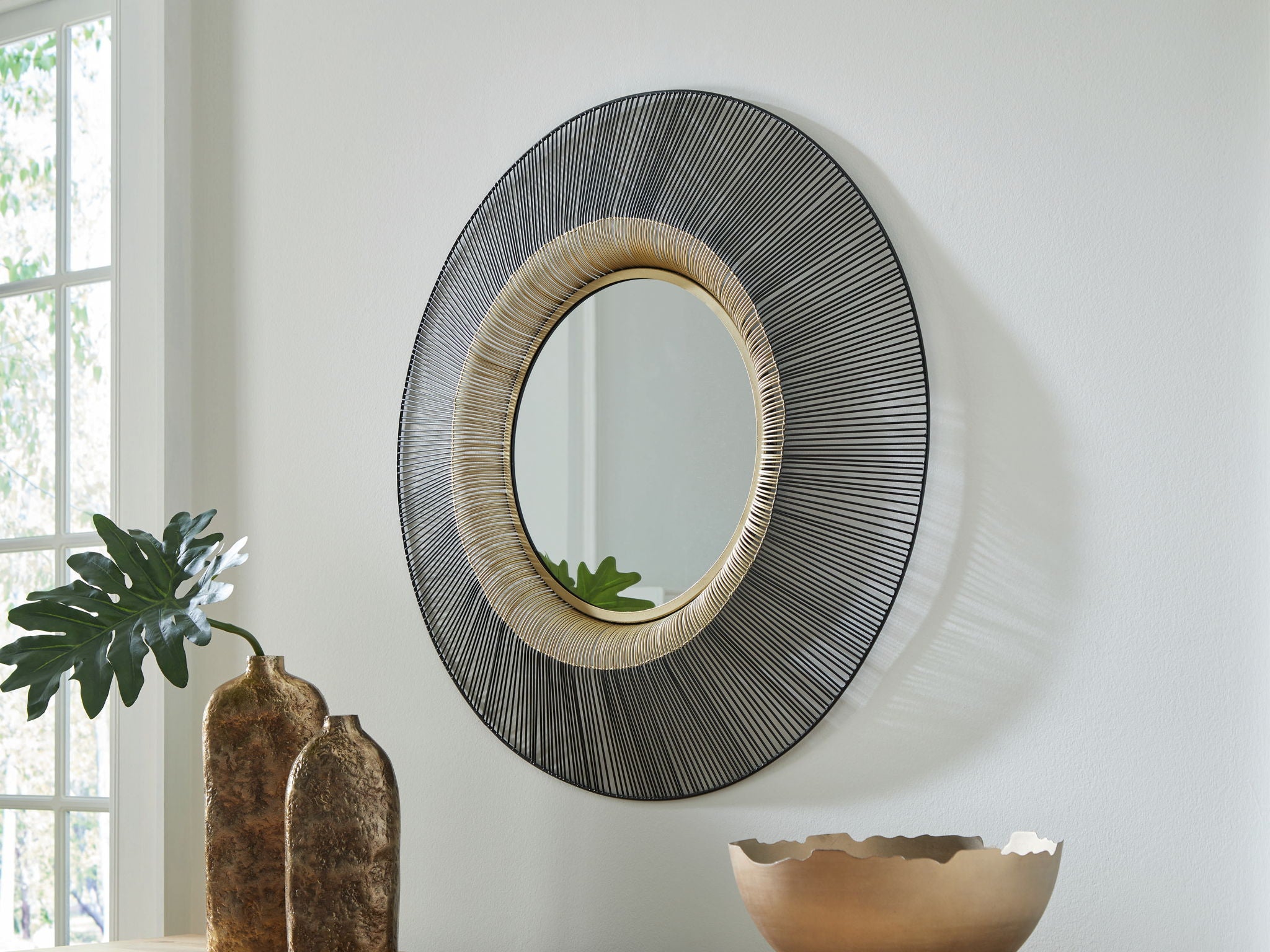 Round accent mirror with black textured outer ring and gold-toned inner bezel