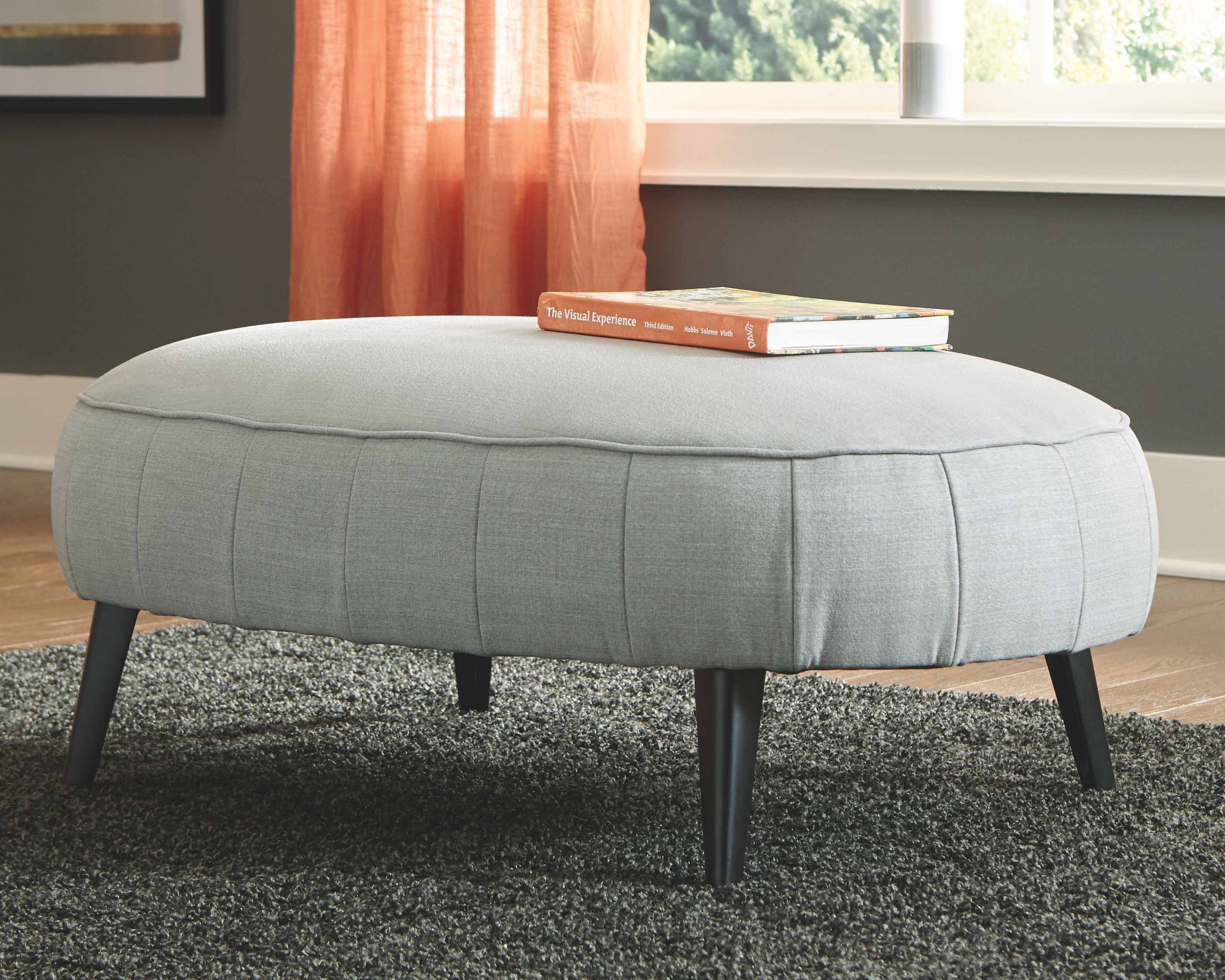 Gray upholstered accent ottoman with stitched top and four tapered legs