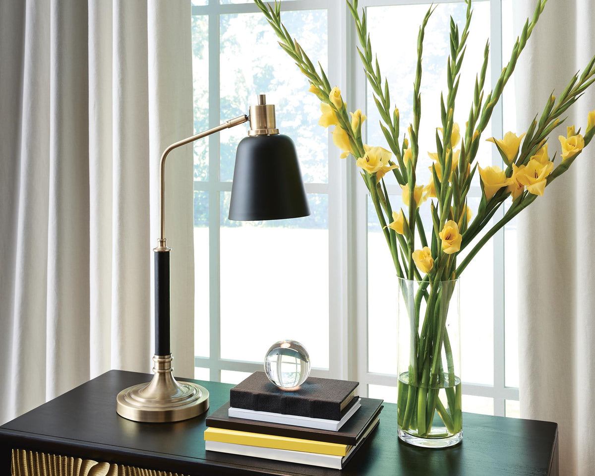 Black cone shade lamp with brass curved arm and round base on tabletop
