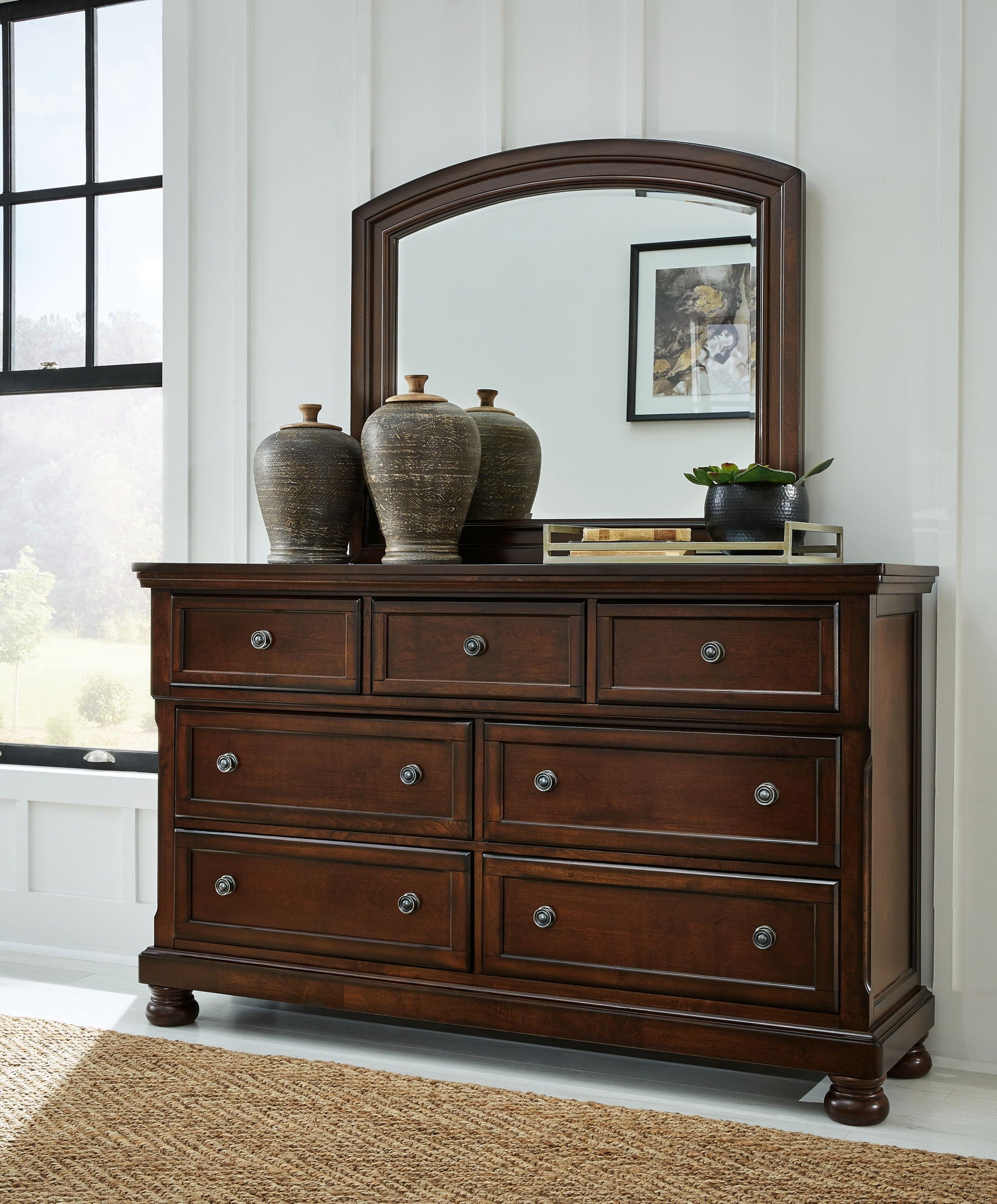 Dark brown dresser with arched mirror and six drawers with round metal knobs