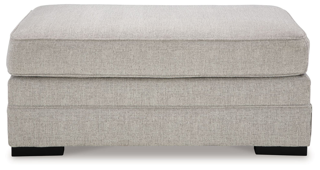 Light gray upholstered ottoman with wide padded top and black block feet