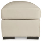 Almond square ottoman with rounded lid, stitched edging, and dark base supports.