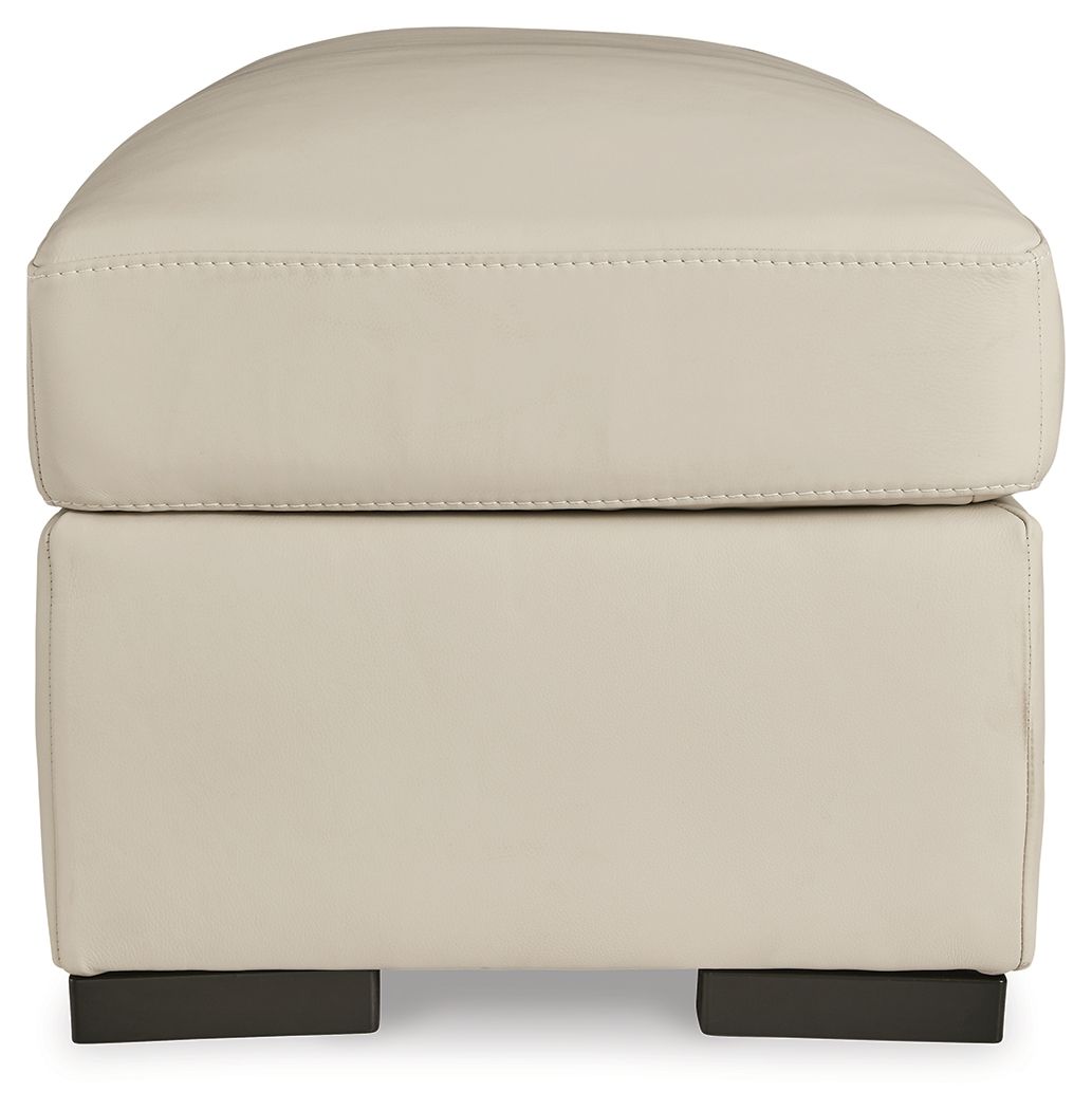 Almond square ottoman with rounded lid, stitched edging, and dark base supports.
