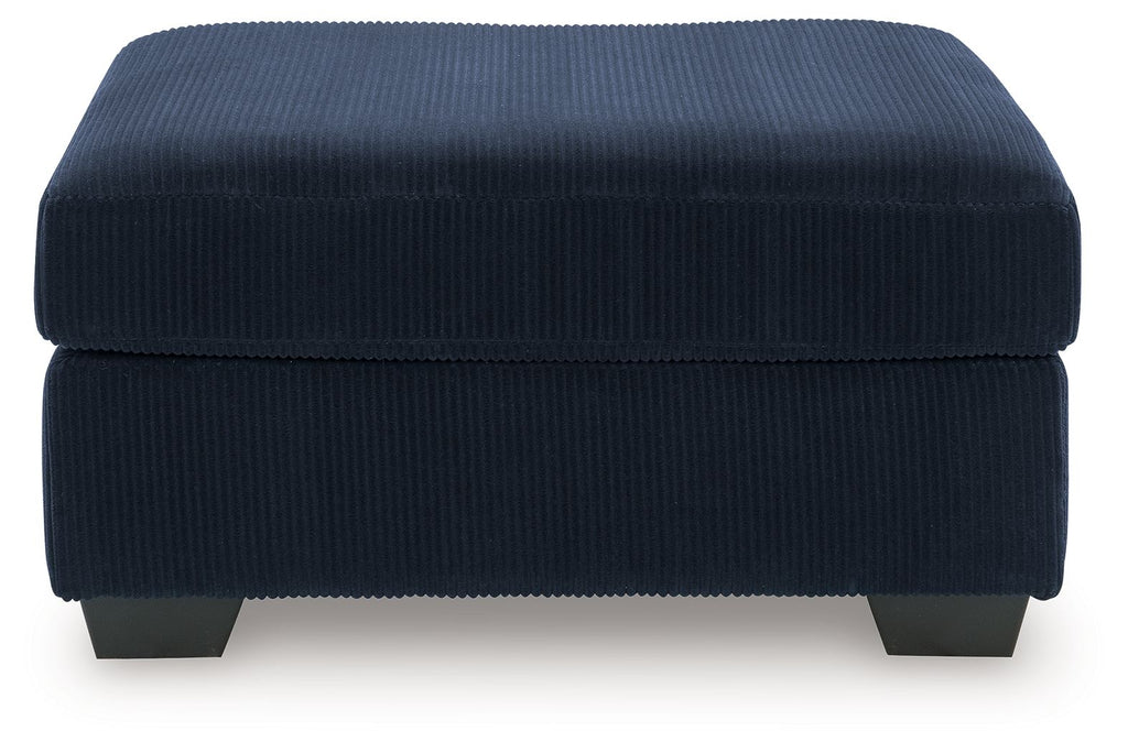 Blue ottoman with ribbed fabric, rounded padded top, dark legs.