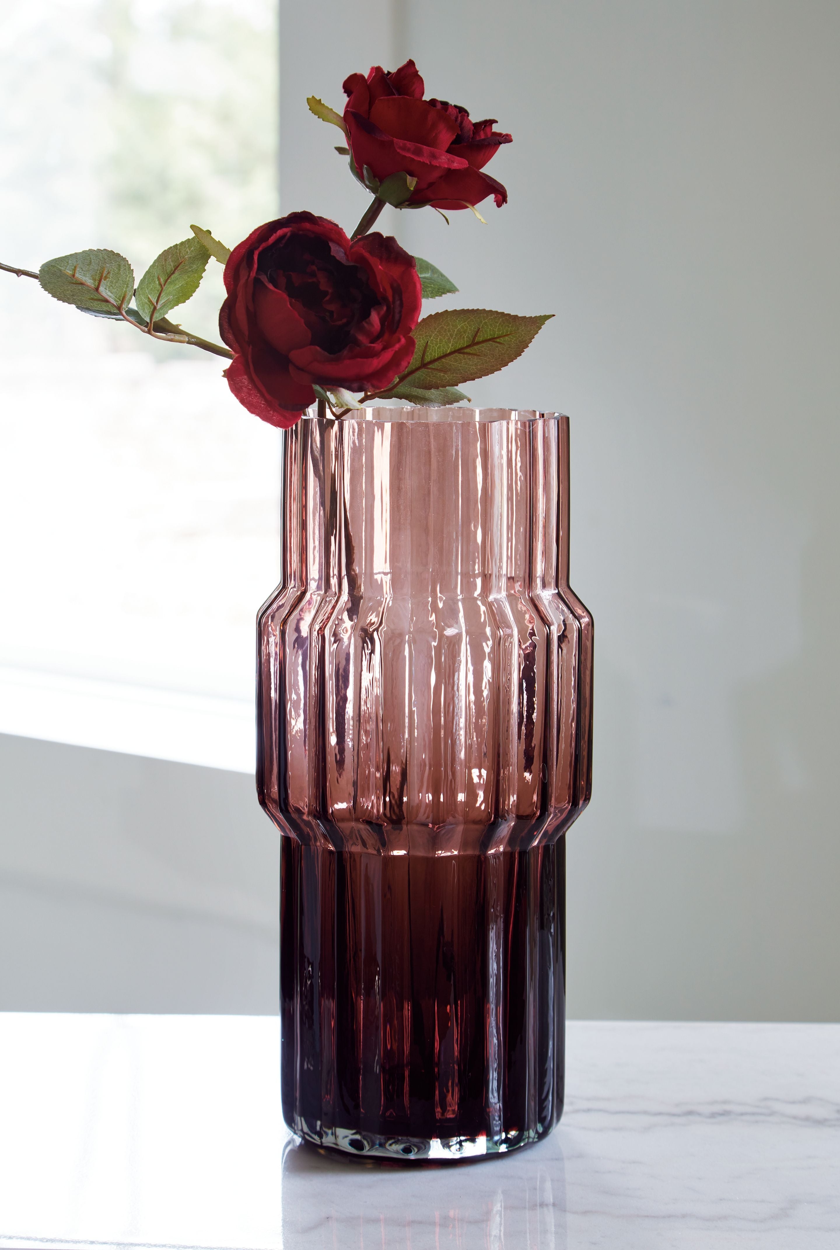 Purple faceted glass vase with ribbed sides holding red roses
