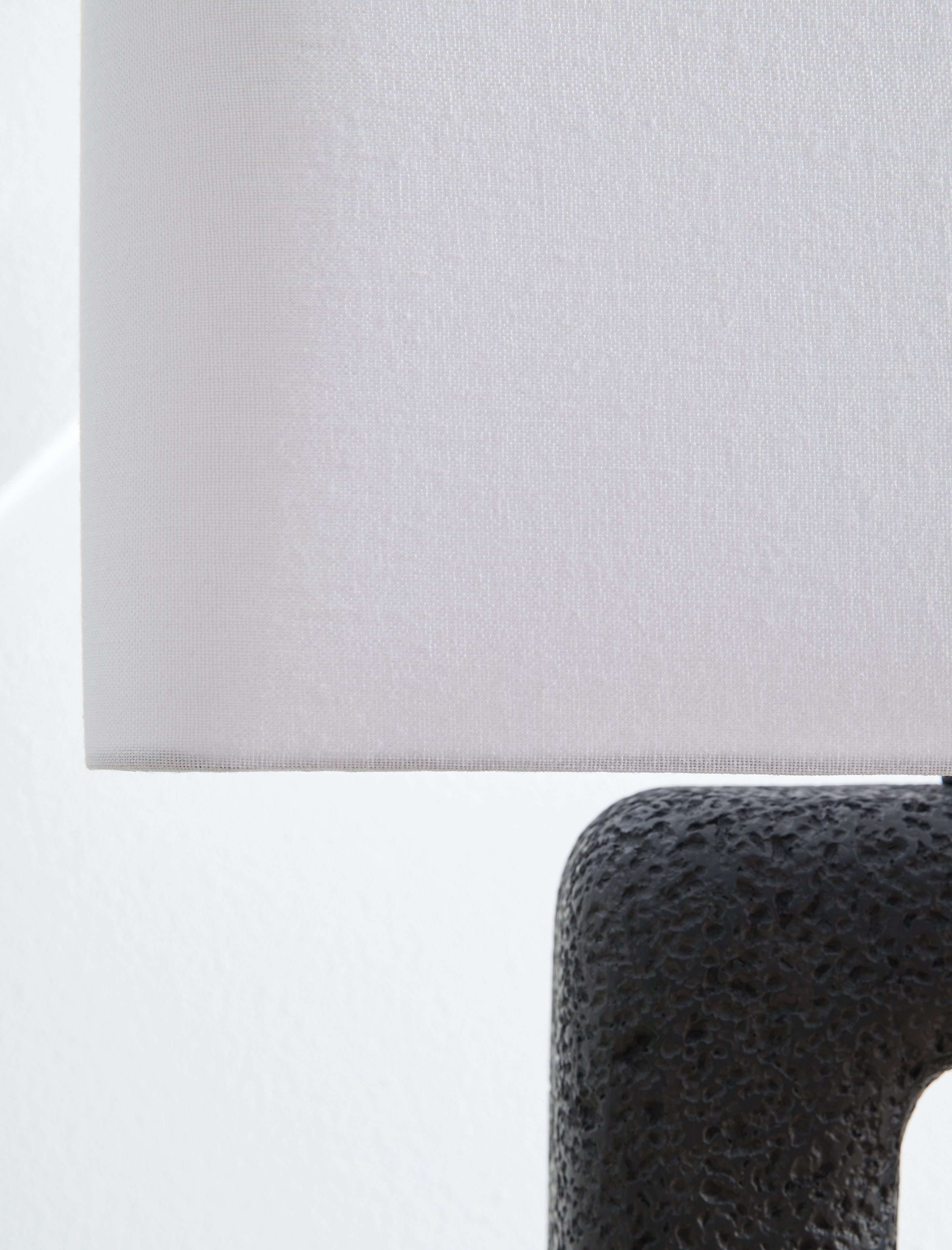 Light fabric lampshade edge over black textured lamp base