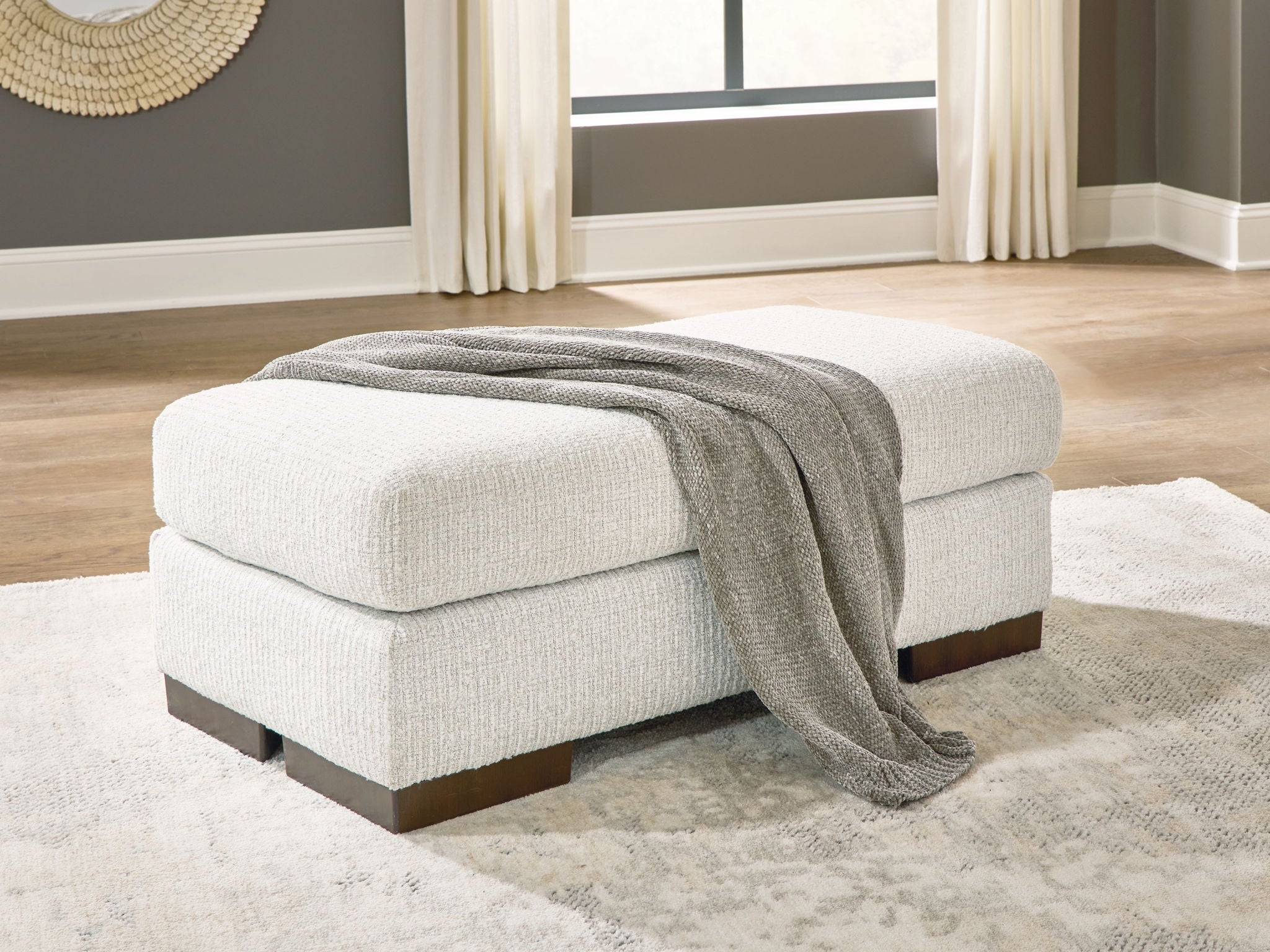 Cream upholstered ottoman with dark wooden legs, gray throw blanket draped on top