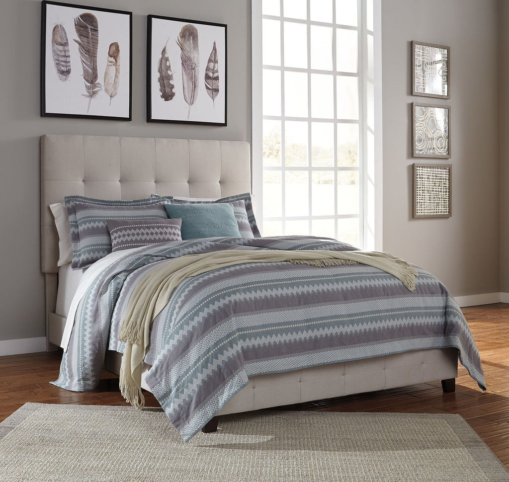 Gray upholstered queen bed with tufted headboard and layered striped bedding