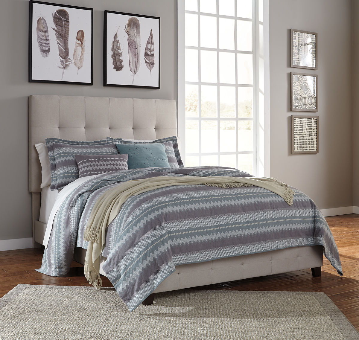 Gray upholstered queen bed with tufted headboard and layered striped bedding