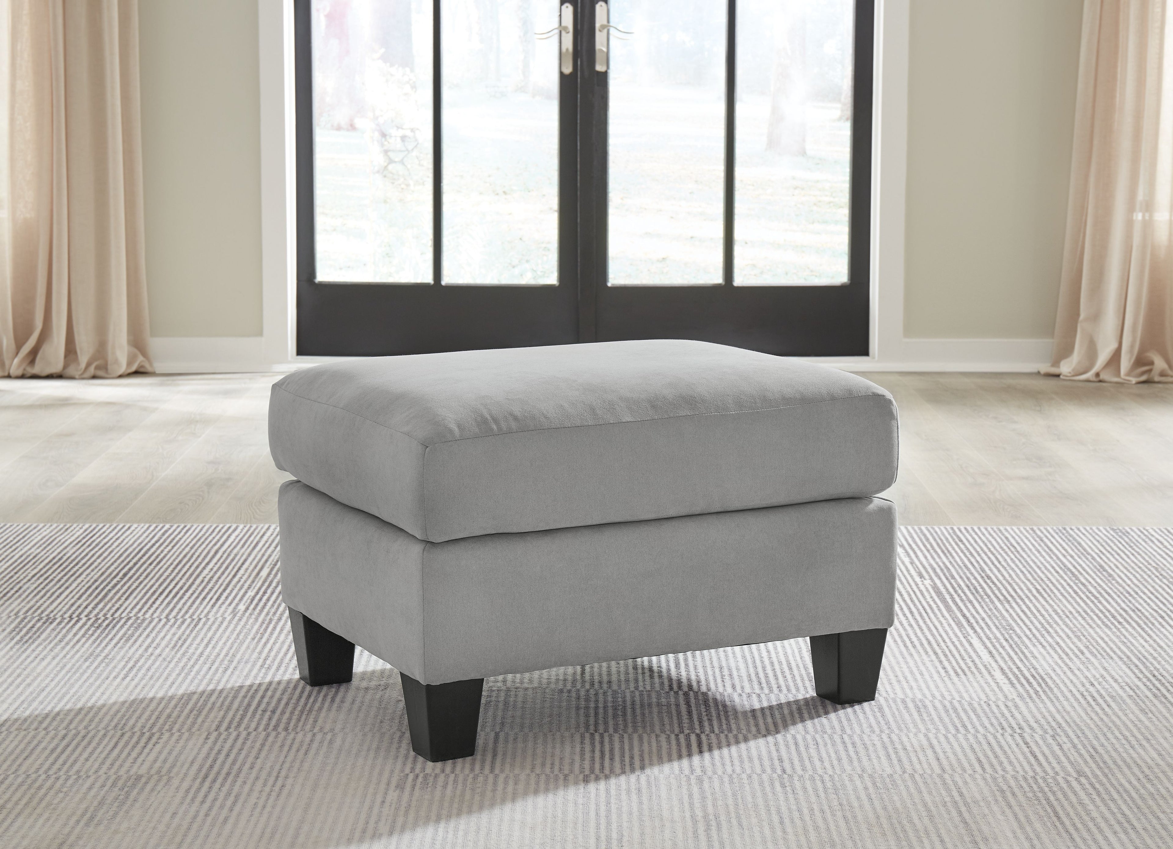 Gray upholstered ottoman with rounded top and dark legs, three-quarter view