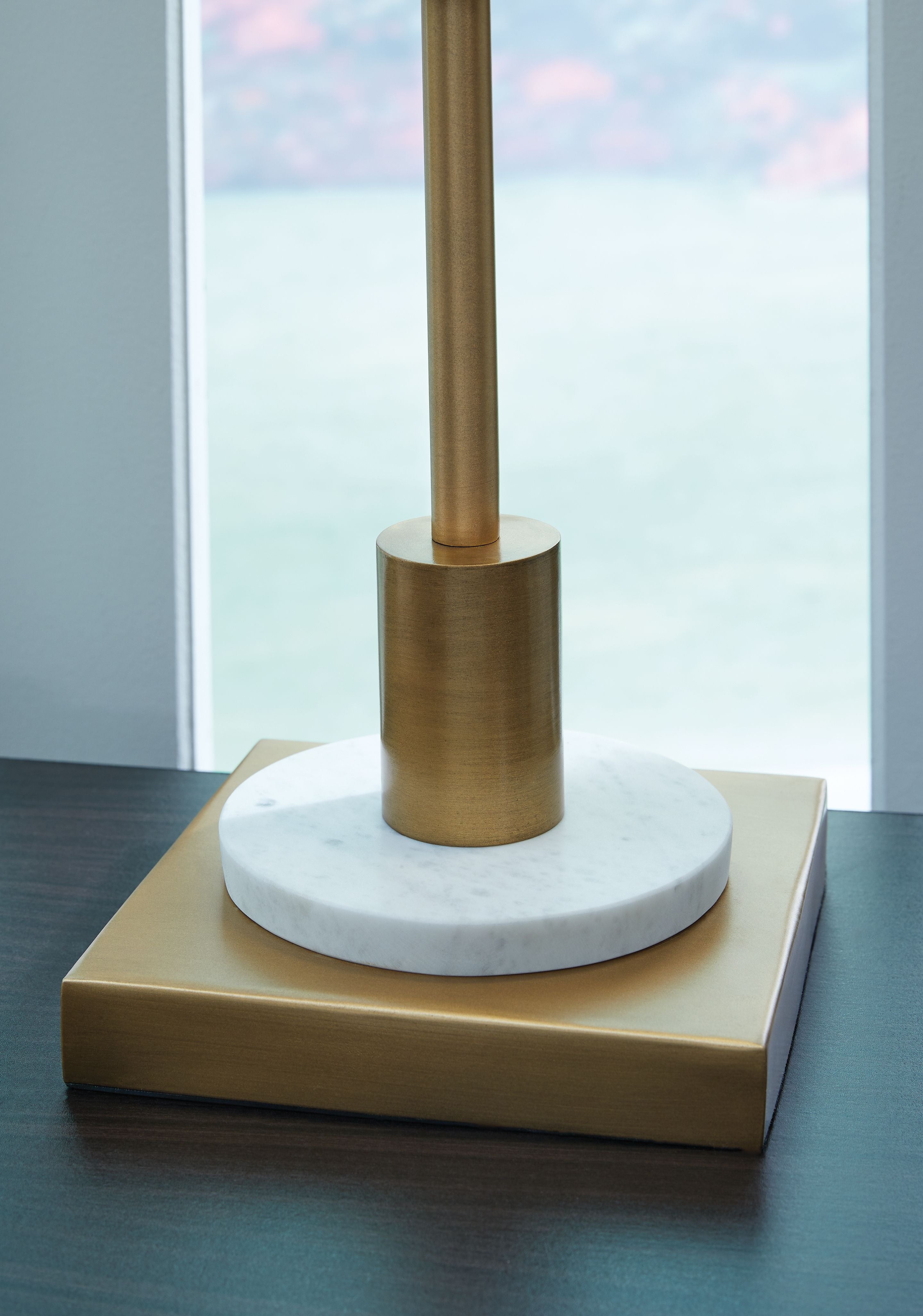 Gold metal lamp base with round marble-like top and tall cylindrical stem, white shade edge