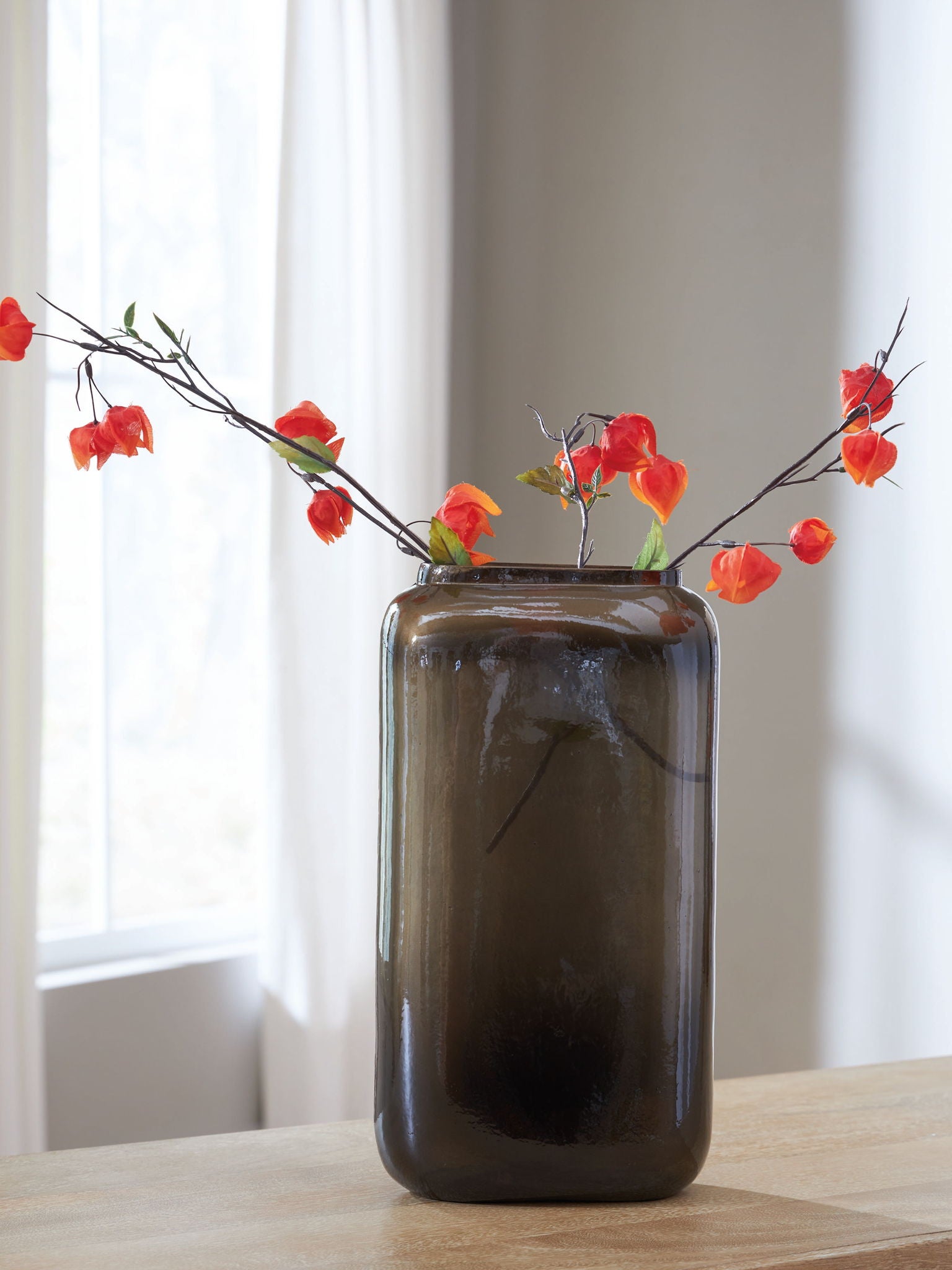 Sumner vase with dark brown glossy glass and red flower stems arranged in it
