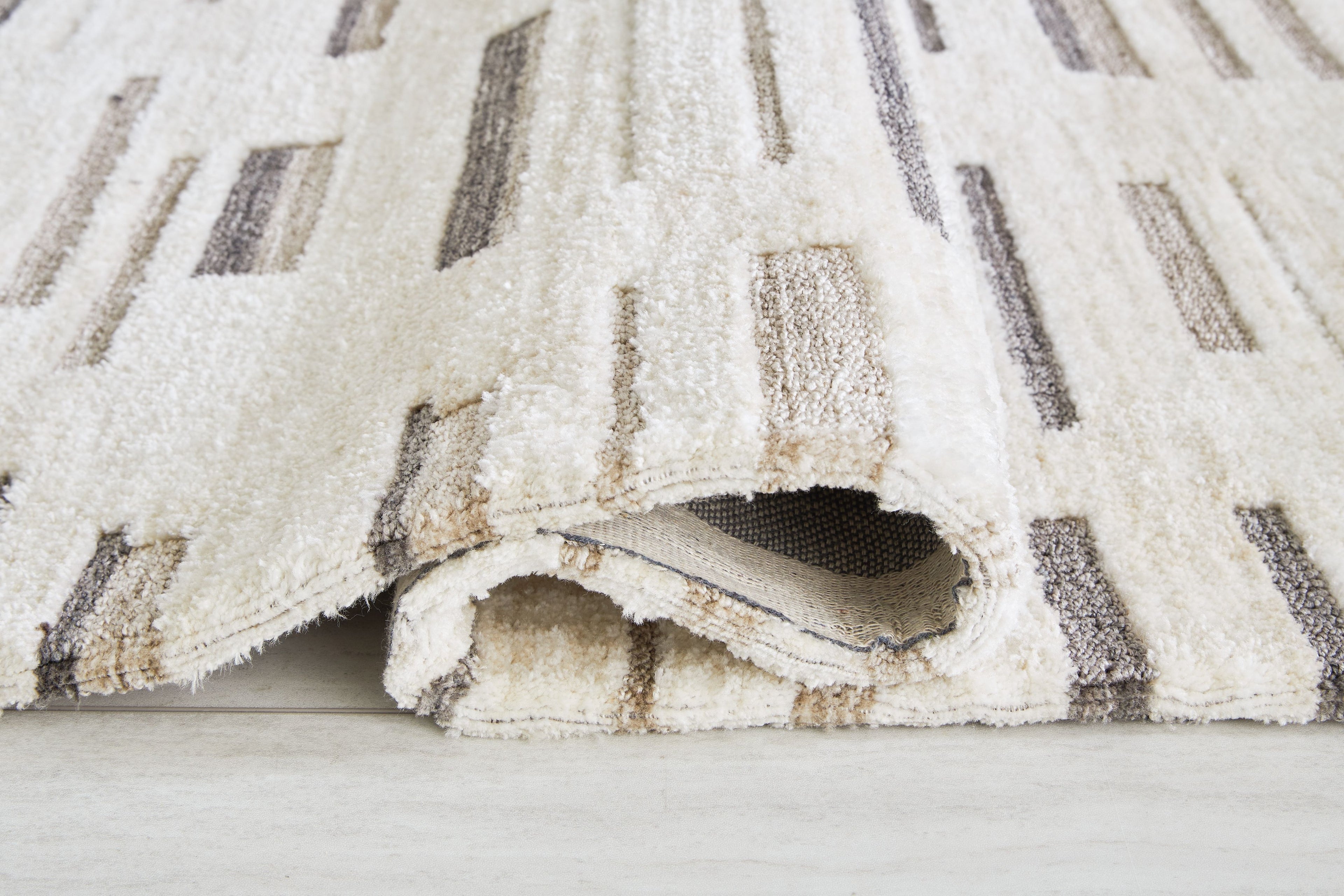 Pearl silver rug corner with textured edge and dark gray stripe motif