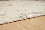 Beige rug corner with textured weave and short fringed edge on floor
