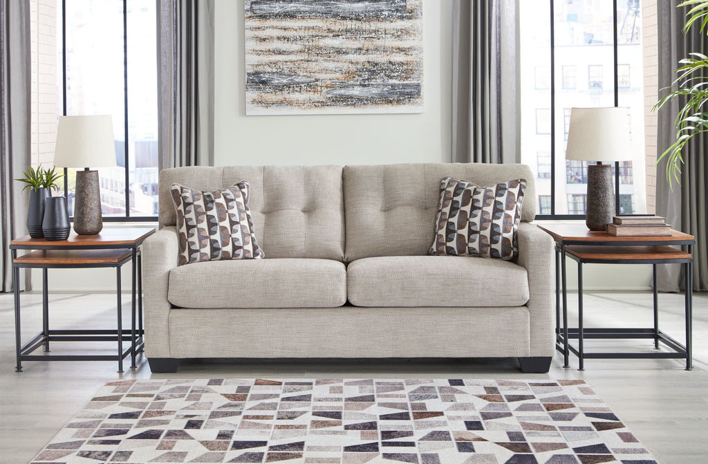 Light gray fabric sofa with two square patterned pillows and tufted back cushions