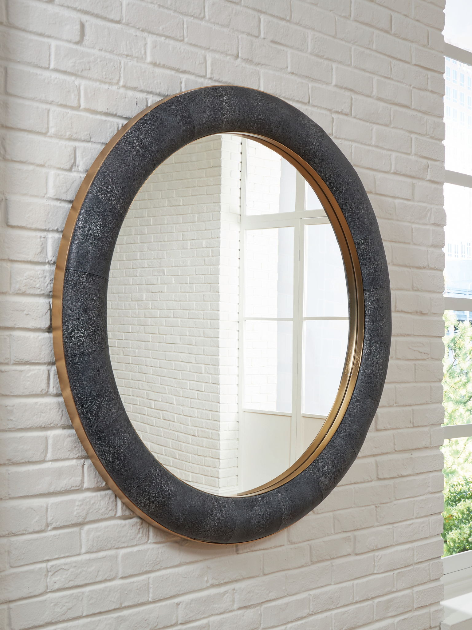Charcoal accent mirror with brass rim mounted on white brick wall