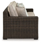 Brown wicker sofa armchair with beige back cushions and folded throw blanket