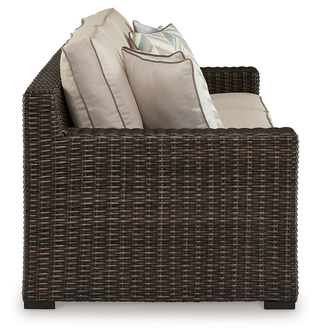Brown wicker sofa armchair with beige back cushions and folded throw blanket