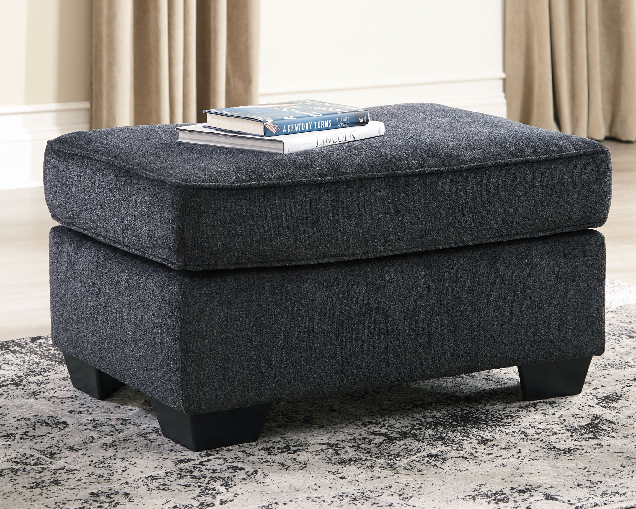Dark gray upholstered ottoman with cushioned top and low block feet