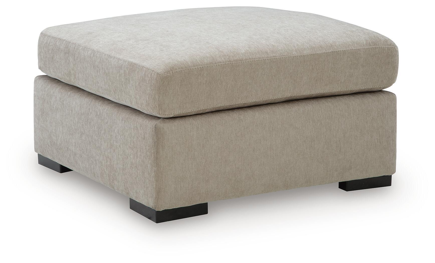 Oversized accent ottoman in light beige upholstered fabric with padded lid and dark block legs.
