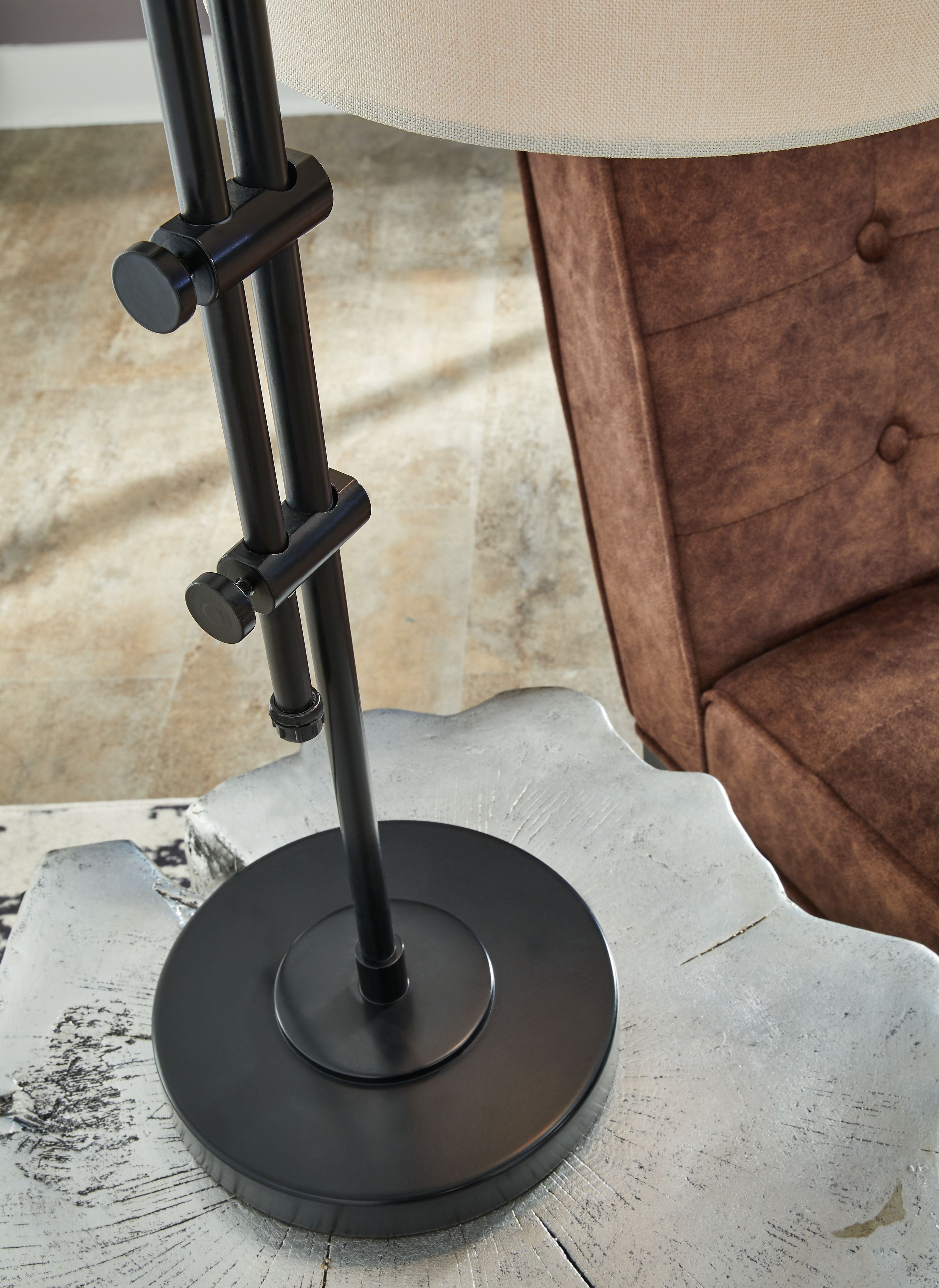Black round base and vertical metal pole of a floor lamp with fabric shade
